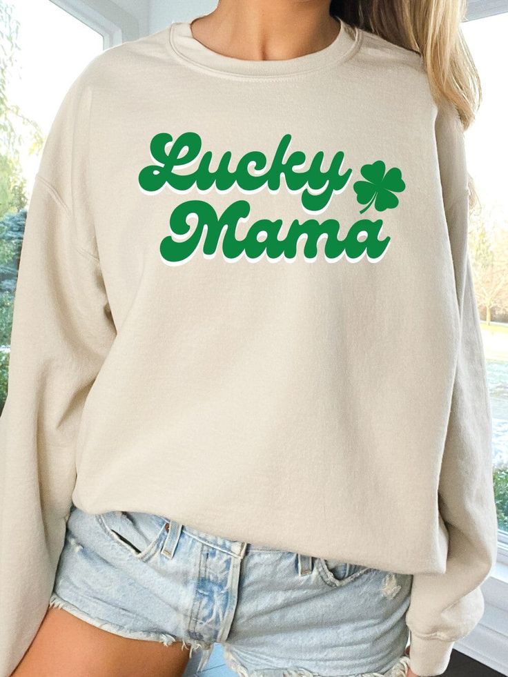 Stay warm and stylish with our Lucky Mama Women's Crewneck Sweatshirt. Featuring the words "Lucky Mama" written in a green and white retro font and a 4-leaf clover design, this sweatshirt is perfect for celebrating St. Patrick's Day or showing off your Irish heritage. Made with a high-quality Gildan Heavy Blend fabric, this sweatshirt is both durable and comfortable. Available in 3 classic colors and 6 sizes, it's perfect for any women. The crewneck design and relaxed fit make it perfect for lou Green Long Sleeve Sweatshirt With Lettering, Green Long Sleeve Slogan T-shirt, Green Long Sleeve T-shirt With Slogan, Green Crew Neck Sweatshirt With Lettering, Green Letter Print Top For St. Patrick's Day, Green Long Sleeve Tops With Name Print, Green Long Sleeve Tops For Mother's Day, Retro Green Slogan Top, Green Relaxed Fit Top With Lettering