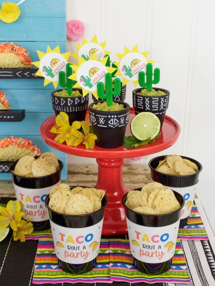 a table topped with cups filled with taco and chips next to other desserts