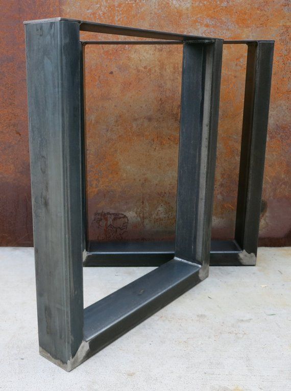 two metal frames sitting next to each other on a cement floor in front of a rusted wall