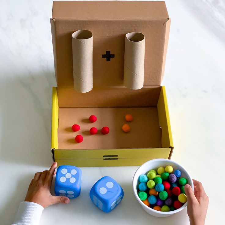 two hands are holding dices in front of a box with candy balls and other items