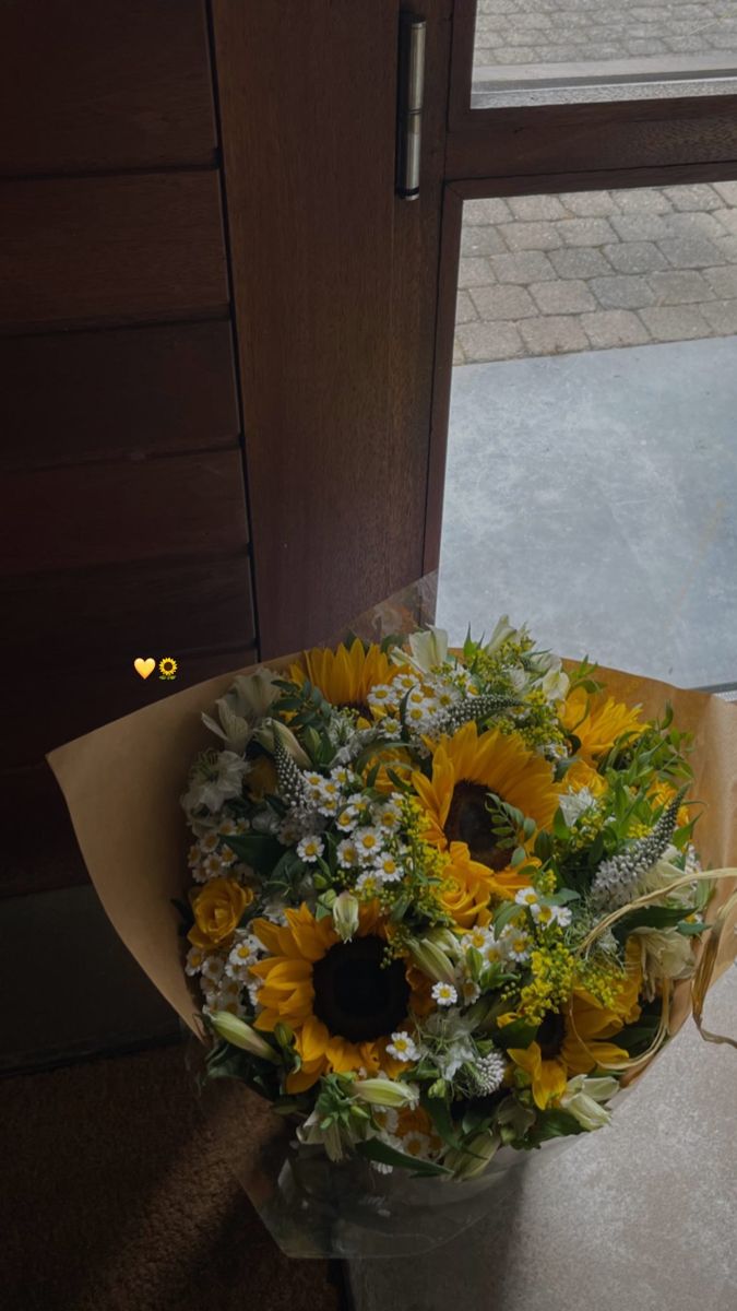 a bouquet of sunflowers and daisies sits in front of a door on the sidewalk