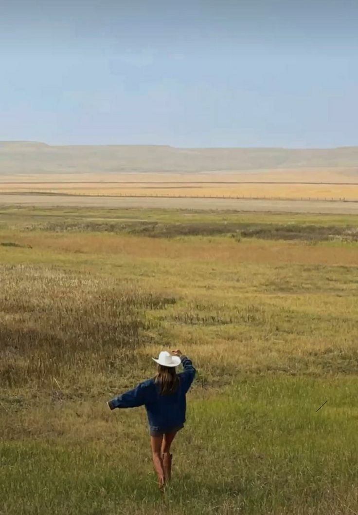 a woman in a blue dress and hat flying a kite on an open field with mountains in the background