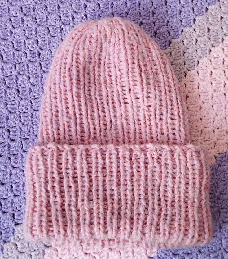 two crocheted hats laying on top of a purple and white blanket next to each other