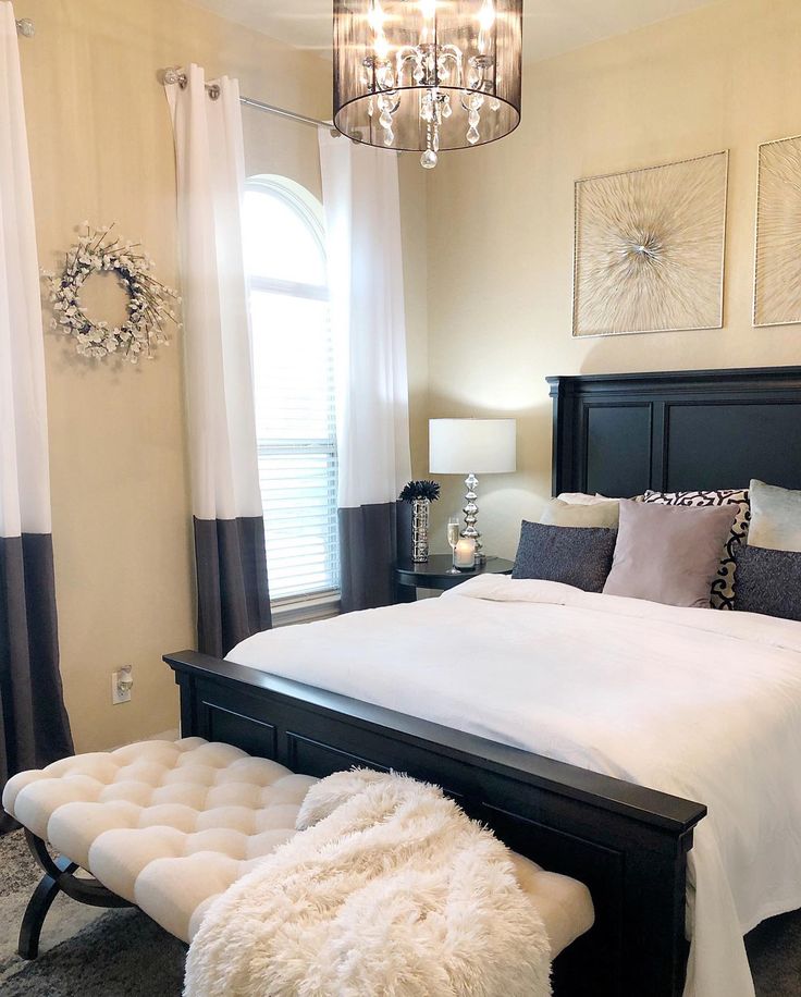 a bedroom with a large bed, chandelier and two windows in the background