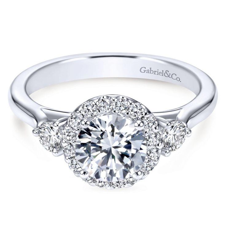 a white gold engagement ring with three round diamonds on the band and an halo setting