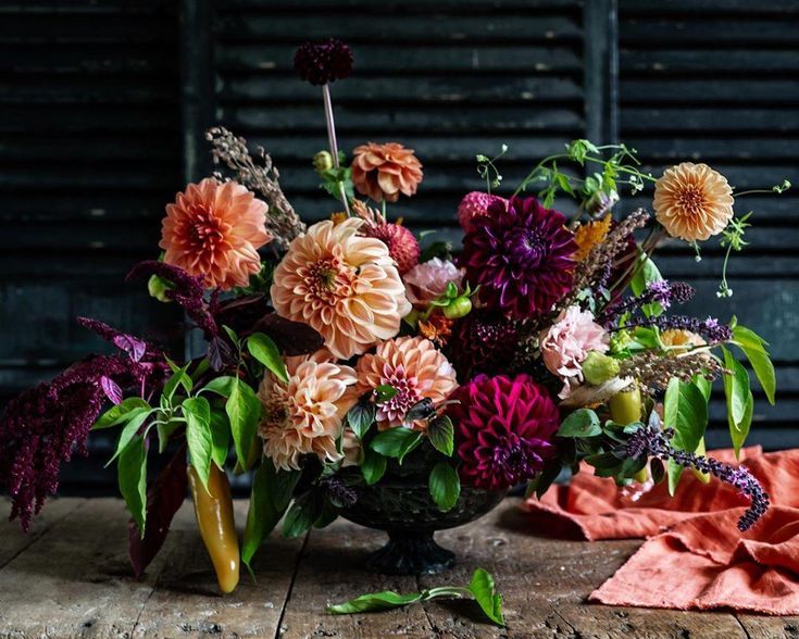 a vase filled with lots of colorful flowers on top of a wooden table next to an orange cloth