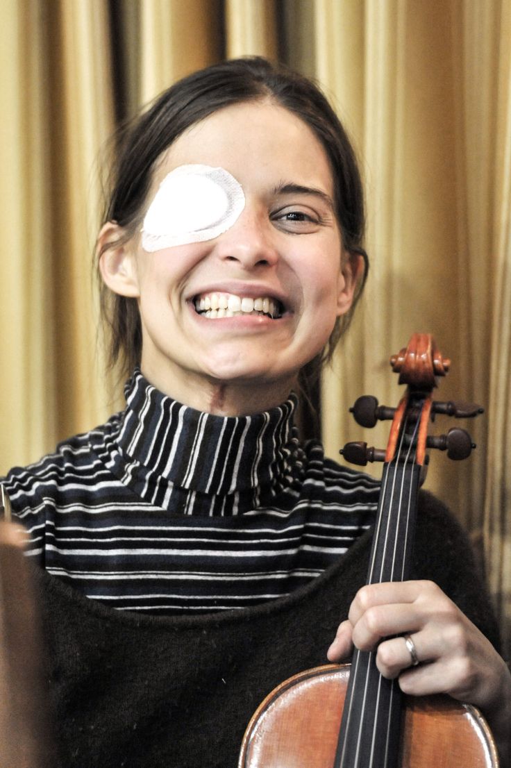 a woman holding a violin and smiling with her eye patch on top of her face