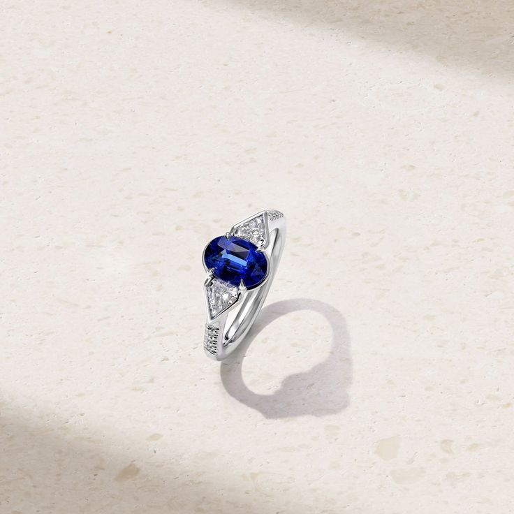 A modern statement piece, this ring showcases a three stone arrangement highlighted by a vibrant sapphire nestled amongst a pair of dazzling fancy cut diamonds. The center stone rests in prongs and is traced by a bezel-like border that extends and cradles the accompanying diamonds. Additional petite round diamonds cascade down along each side of the shank for additional sparkle. A true one-of-a-kind heirloom, wear yours solo for an impactful look. Metal: 18kt Gold Sapphire Weight: 2.18 ct. Fancy Luxury Three Stone Round Cut Sapphire Ring, Luxury Sapphire Ring With Marquise Cut, Sapphire Three Stone Diamond Ring, Luxury Three Stone Sapphire Promise Ring, Luxury Three-stone Sapphire Promise Ring, Fine Jewelry Three-stone Sapphire Ring, Formal Three Stone Lab-created Sapphire Ring, Formal Three Stone Sapphire Ring With Lab-created Sapphire, Three Stone Lab-created Sapphire Ring For Formal Occasions