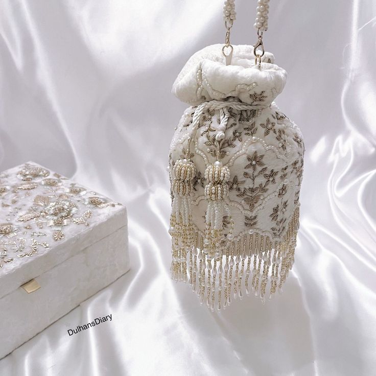 Elevate your bridal ensemble with our exquisite Ivory Bridal Wedding Day Potli Bag. Crafted from luxurious velvet fabric, adorned with intricate zardozi embroidery, this potli bag exudes elegance and opulence. The delicate beadwork adds a touch of glamour, while the beautiful log tassels at the bottom enhance its regal charm. Complete with a beaded latkan and a beaded strap, this potli bag is the perfect accessory to complement your bridal look, adding a timeless allure to your special day. Product Details: *Handmade with traditional Pakistani and Indian techniques *Spacious interior  *Measures 6 inches To explore additional styles, kindly visit our website at dulhansdiary.etsy.com. . . . . . . #Ivorypotlibag #handmadeclutch #bridalhandbag #weddingaccessories #ethnicbag #uniquegift #artisa Bridal Pouches Pakistani, Elegant Bags For Festivals And Receptions, White Festive Clutch For Party, White Clutch For Wedding And Festivals, Elegant Evening Bag For Receptions And Festivals, Elegant Bags For Reception And Festivals, Festive White Clutch For Party, Elegant Potli Bag With Pearl Handle, Elegant Potli Bag For Festivals And Receptions