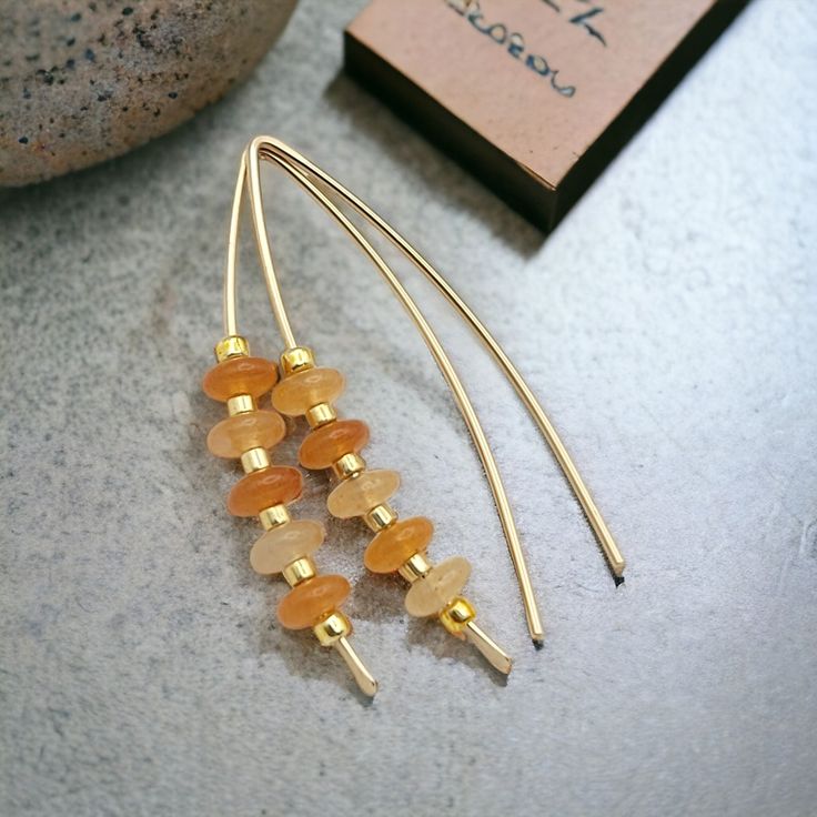 Indulge in luxury with our Wish - Orange Aventurine & Gold earrings. Handcrafted with golden threads and shimmering orange aventurine gemstones, these earrings add a touch of sophistication to any outfit. The perfect accessory to match Pantone's 2024 color of the year, Peach Fuzz. 14k Gold Filled wire Natural Orange Aventurine Gemstones Approximately 1.5" long Includes Silicone Backing Nut Sent in a Ribboned Gift Box with Polishing Cloth Handmade in Montana Gold Aventurine Earrings Gift, Gold Carnelian Earrings With Ear Wire, Carnelian Gold Earrings With Ear Wire, Orange Earrings With Gold Beads As A Gift, Orange Earrings With Gold Beads For Gift, Orange Aventurine, 2024 Color, African Turquoise, Peach Fuzz