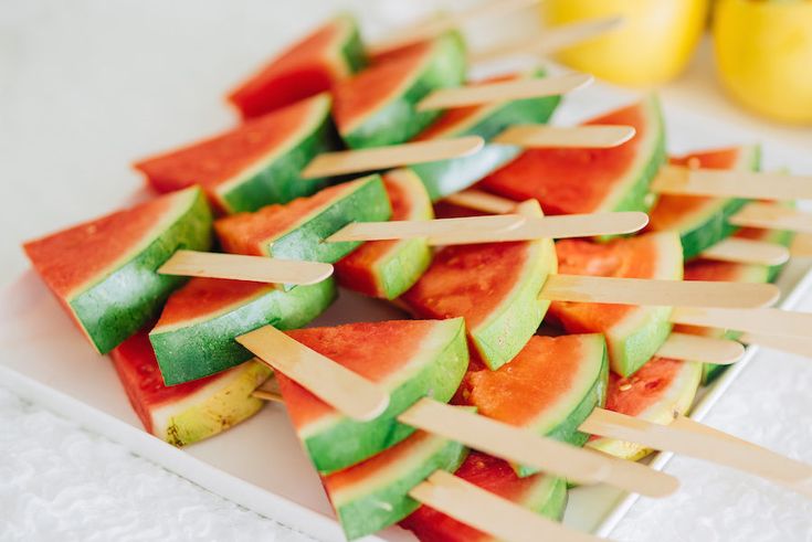 watermelon and apple skewers are arranged on a white platter with lemons in the background