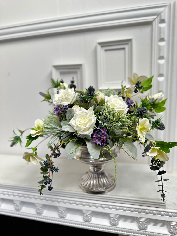 a vase filled with white and purple flowers on top of a table next to a mirror