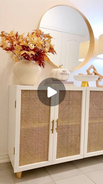 a white cabinet sitting next to a mirror and vase with flowers on top of it