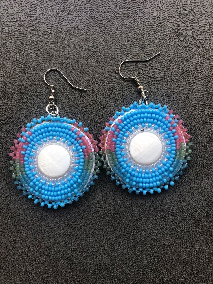 Handmade Native American beautiful mother of pearl center earrings.   Made with size 11 seed beads. The colors are turquoise blue, greasy blue, greasy green, and greasy pink and crystal clear AB (aurora Borealis) The earring measures 1.5 inches round. They are very lightweight and comfortable for wearing all day. They are made with a surgical steel earring hooks   I now offer free shipping on orders $35.00 and over! I ship on monday - Friday except on holidays. If you have any questions or would like additional pictures please message me. Miigwech Artisan Blue Beaded Round Earrings, Blue Round Beaded Earrings, Blue Round Beaded Earrings With Colorful Beads, Handmade Iridescent Round Bead Earrings, Handmade Iridescent Earrings With Round Beads, Turquoise Beaded Round Earrings, Blue Beaded Circle Jewelry, Blue Round Beaded Earrings With Ear Wire, Unique Colorful Beaded Round Earrings