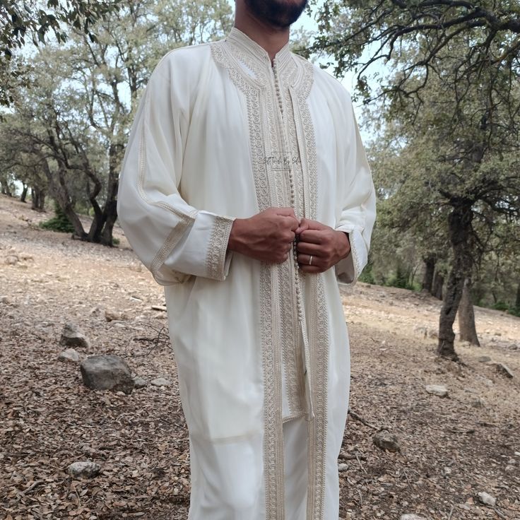 a man standing in the woods with his hands on his hips wearing a white outfit