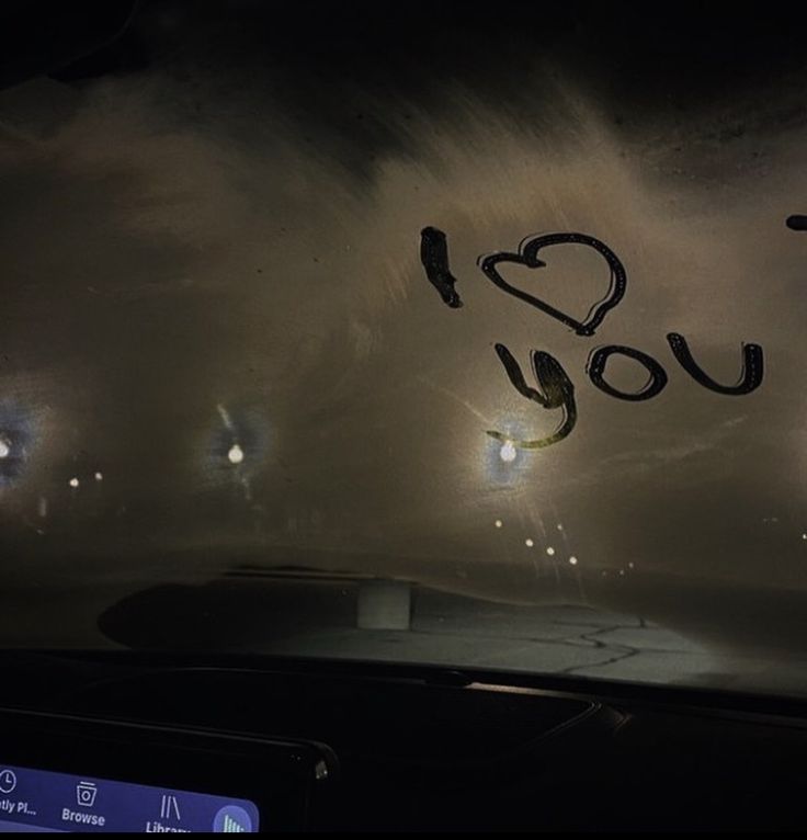 i love you written on the windshield of a car at night with lights in the background