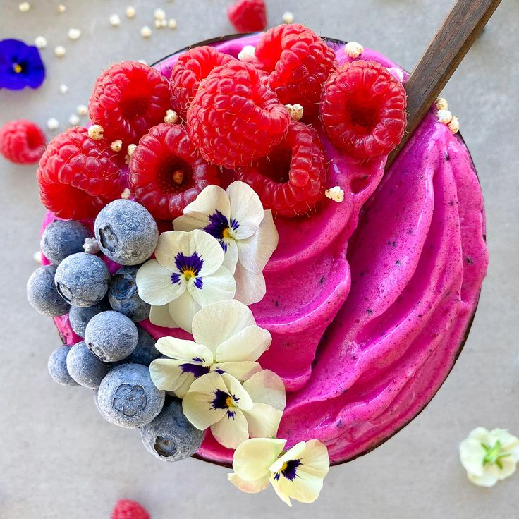 a bowl filled with berries and blueberries on top of a gray table next to flowers