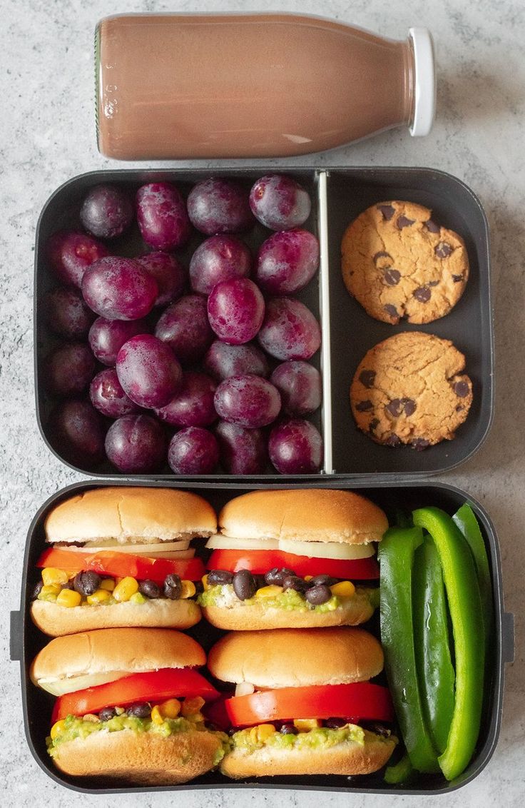 two trays filled with sandwiches and grapes next to cookies, pickles and chocolate chip cookies