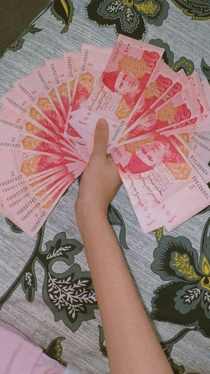 a person is holding five pink bills in their hand and the other one has a fan on it