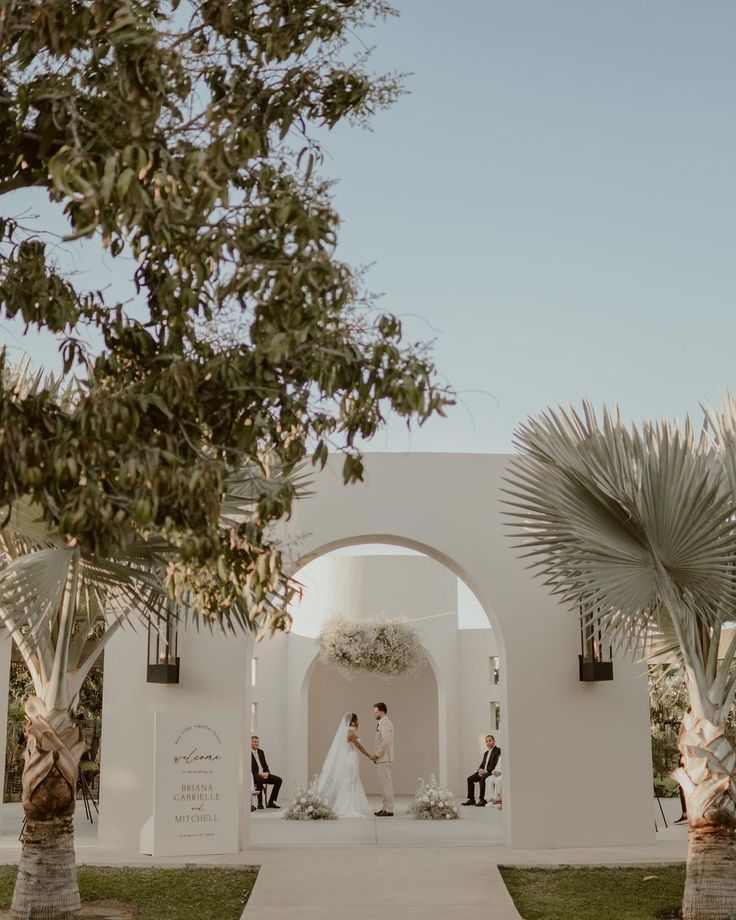 a bride and groom standing in front of an archway with palm trees on either side