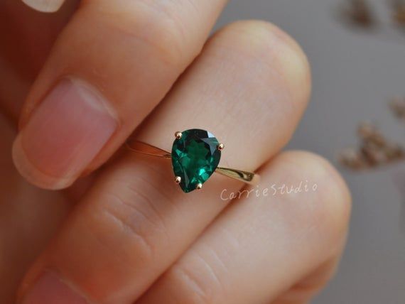 a woman's hand holding a green ring with a heart shaped stone on it