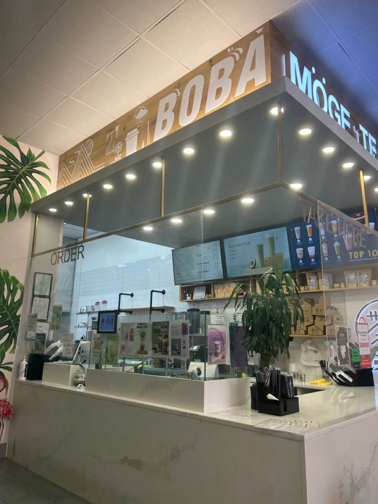 the inside of a coffee shop with lights on and plants in pots behind the counter