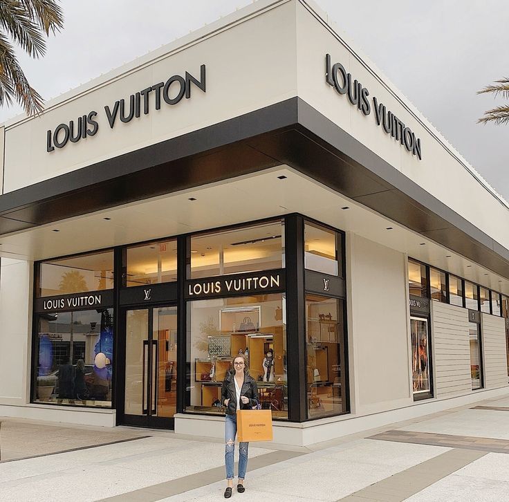 a woman standing in front of a louis vuitton store holding a shopping bag