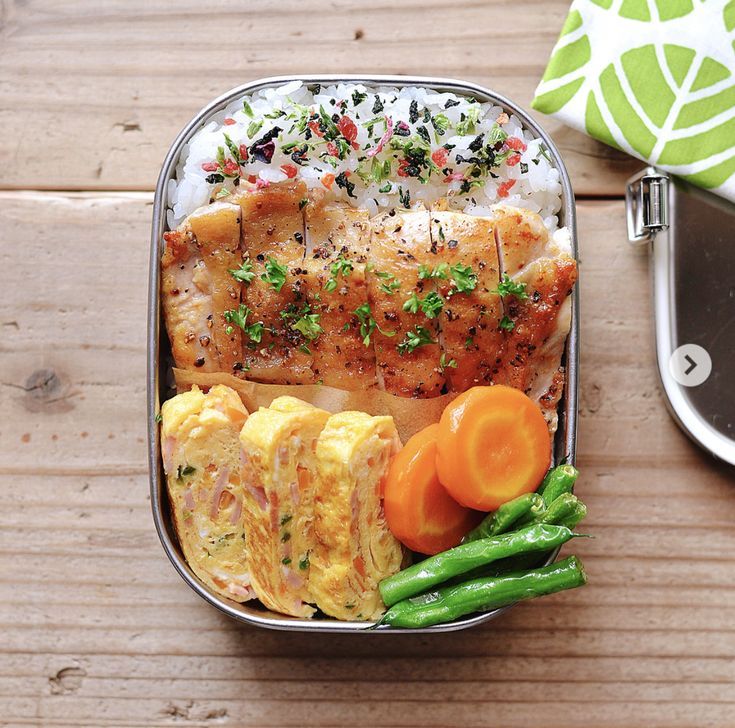 a bento box filled with meat, vegetables and rice on top of a wooden table