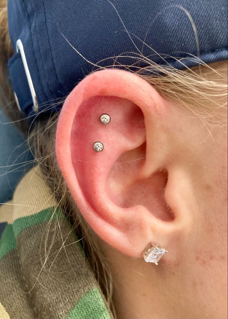 a woman with three piercings on her ear and wearing a baseball cap in the background