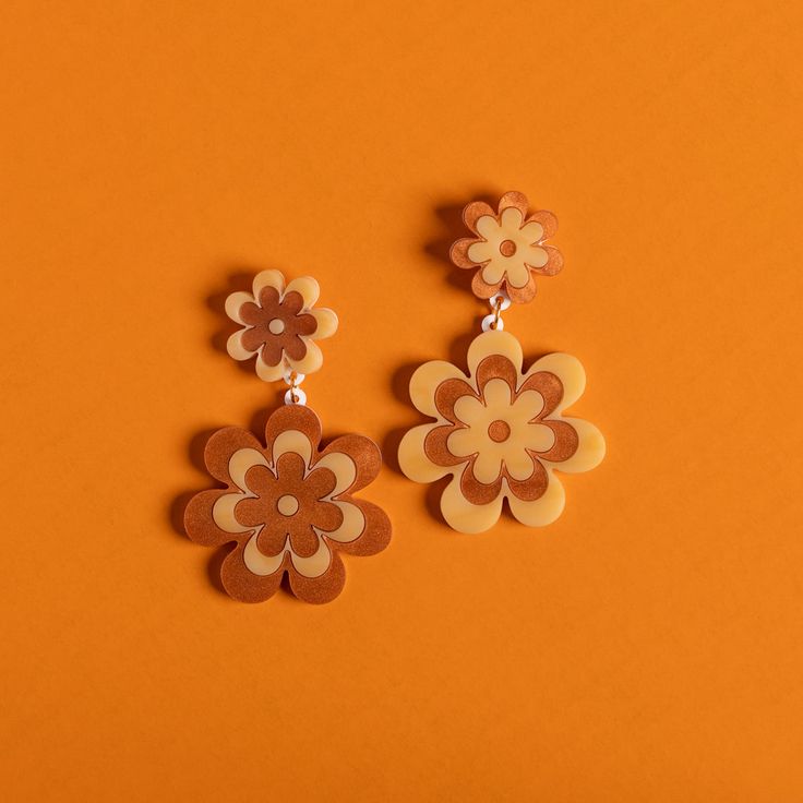 two brown and white flower earrings on an orange background