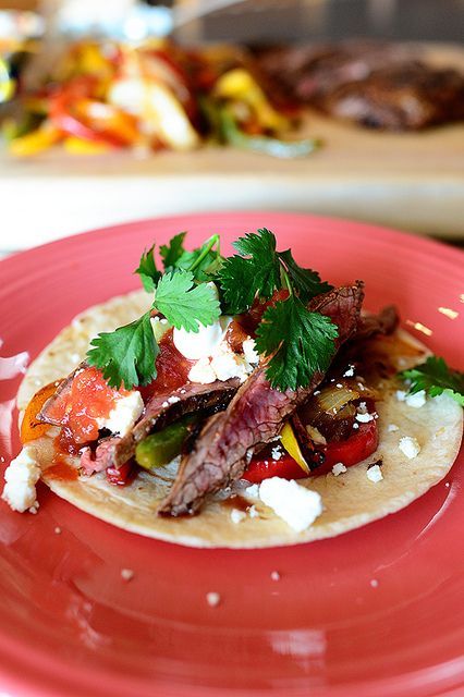 a taco with meat, vegetables and cheese on a red plate in front of other food items