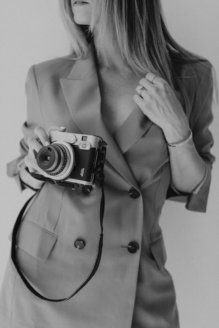 a woman holding a camera in her right hand and wearing a suit on the other