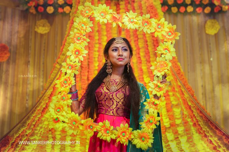 a woman standing in front of a yellow and orange backdrop with flowers around her head