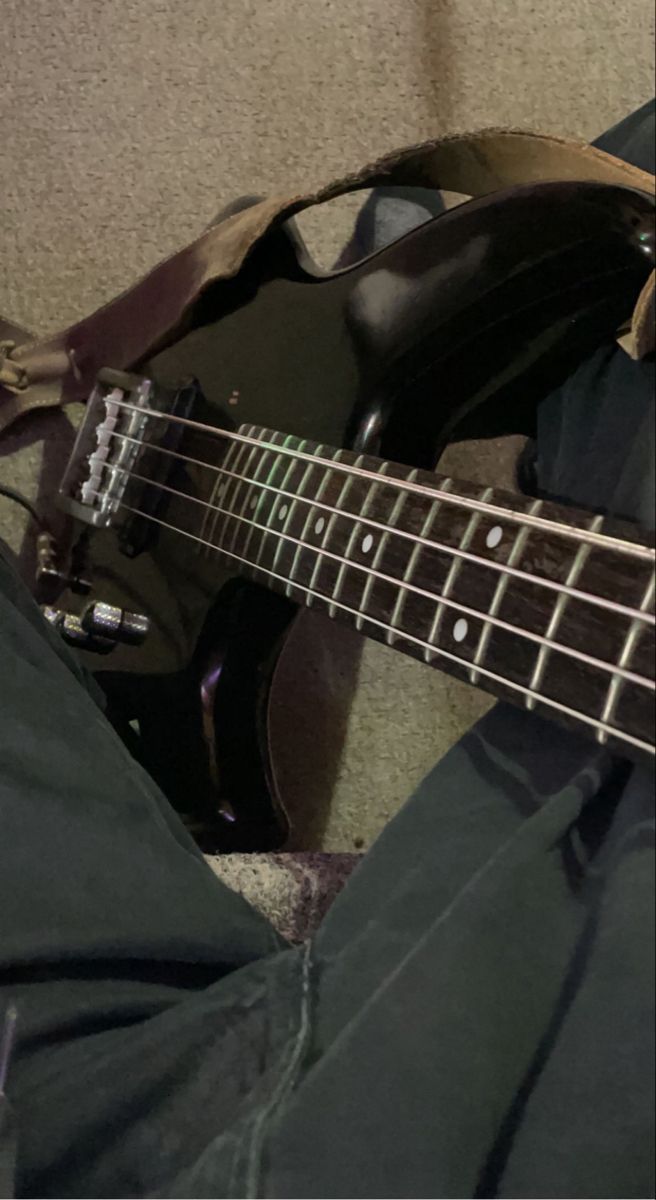 an electric bass guitar laying on the floor next to someone's pants and shoes