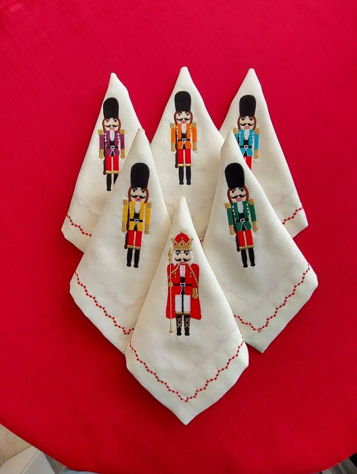 four embroidered tea towels with the image of three royal guards on them, sitting on a red table cloth