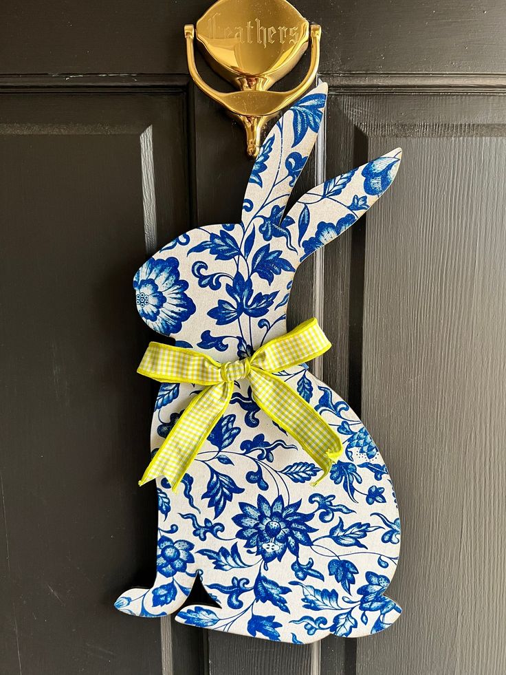 a blue and white bunny door hanger with a yellow bow on it's head