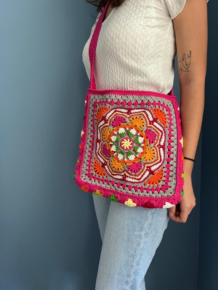 a woman holding a pink crocheted bag with an orange flower on the front