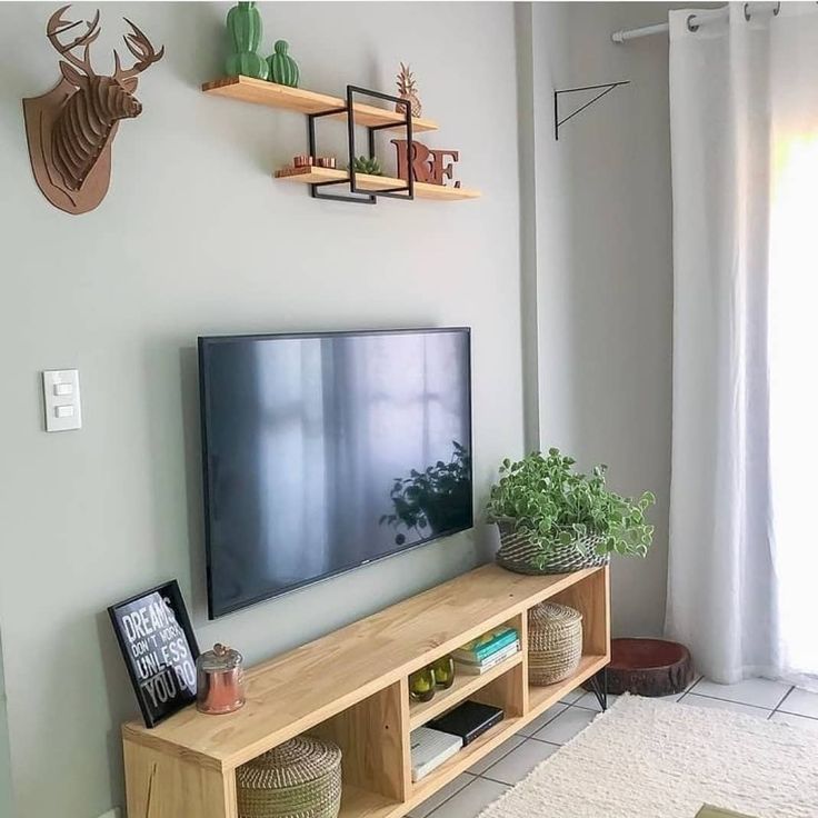 a flat screen tv sitting on top of a wooden shelf in a living room next to a window