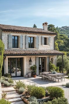 an outdoor patio with tables and chairs next to a stone building surrounded by greenery