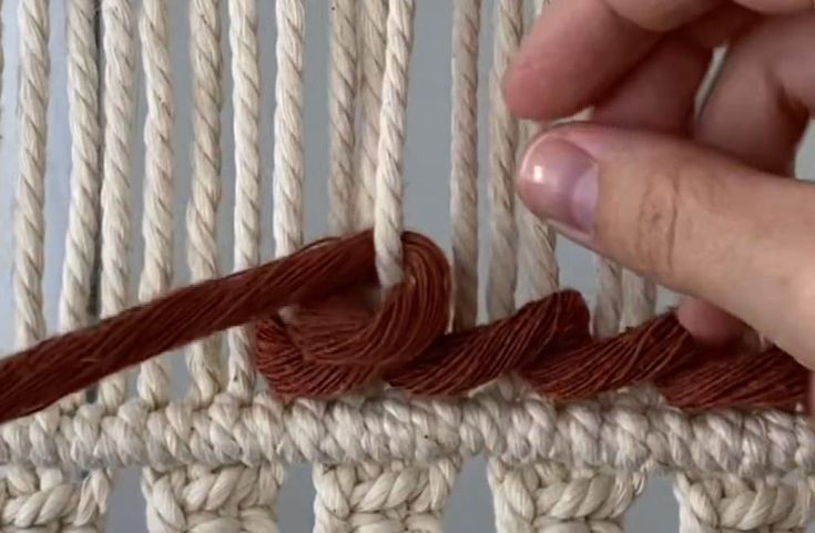 someone is knitting on the loom with red thread and brown yarn in front of them