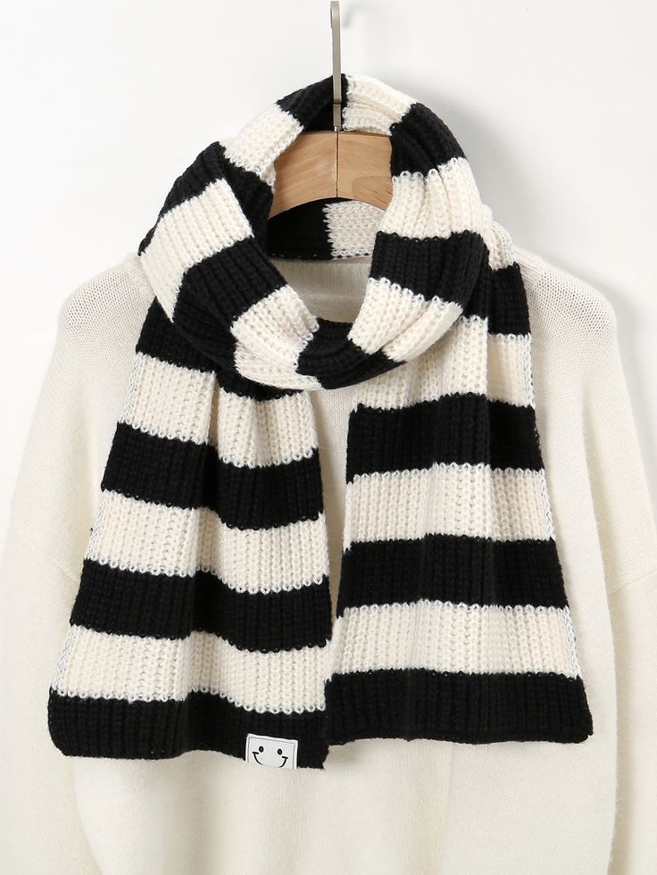 a black and white striped scarf hanging on a hanger in front of a white sweater