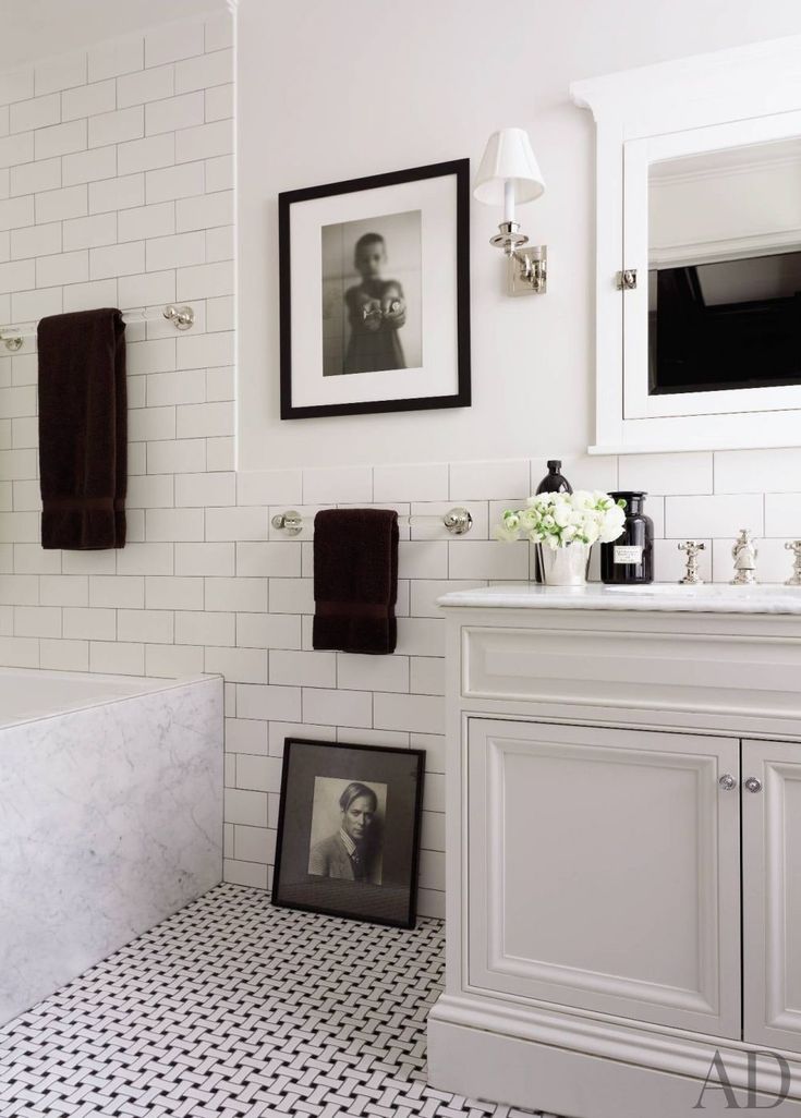 a white bathroom with black and white flooring, framed pictures on the wall above the sink