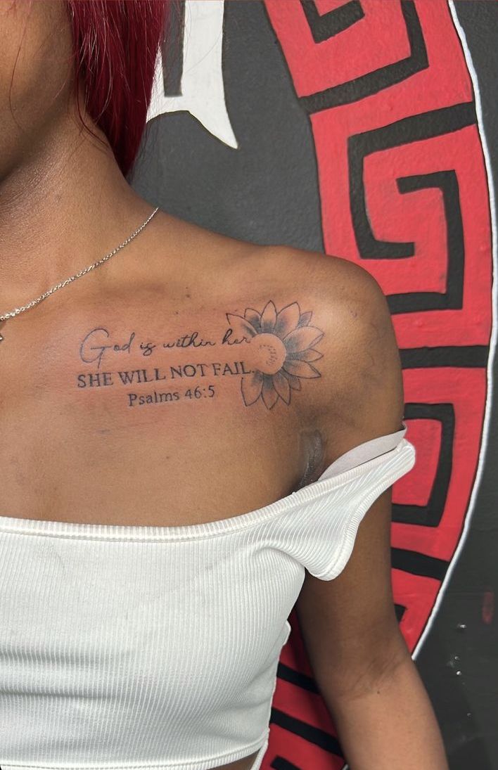 a woman wearing a white top has a tattoo on her left shoulder that says god is with us she will not fail