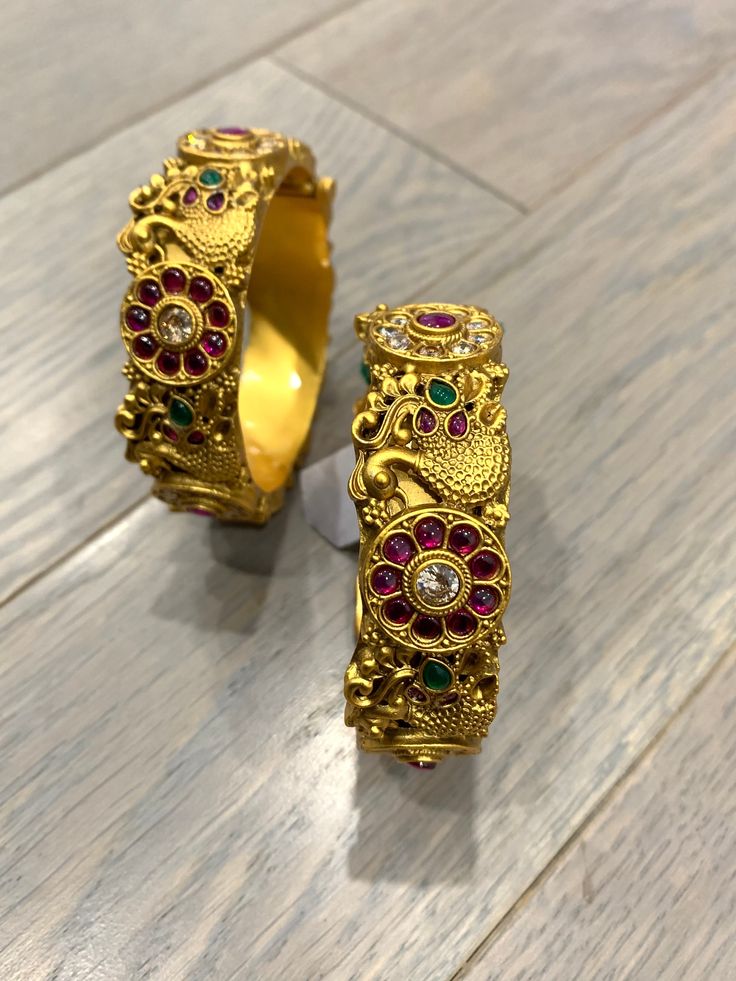 Temple bangle in matte gold and ruby stone. Detailing has the Rajasthani similarity. About an inch wide. Disclaimer: Price listed is for a single Kada. If you want to get them in a pair please select quantity 2. Gold Ruby Bracelet In Temple Jewelry Style, Gold Ruby Bracelets In Temple Jewelry Style, Gold Peacock Design Bracelets For Festive Occasions, Gold Bracelet With Peacock Design For Festive Occasion, Traditional Gold Bangle With Ruby, Gold Bracelet With Peacock Design For Festive Season, Gold Peacock Design Bracelet For Festive Occasions, Traditional Gold Ruby Bangle, Festive Gold Bracelets With Peacock Design