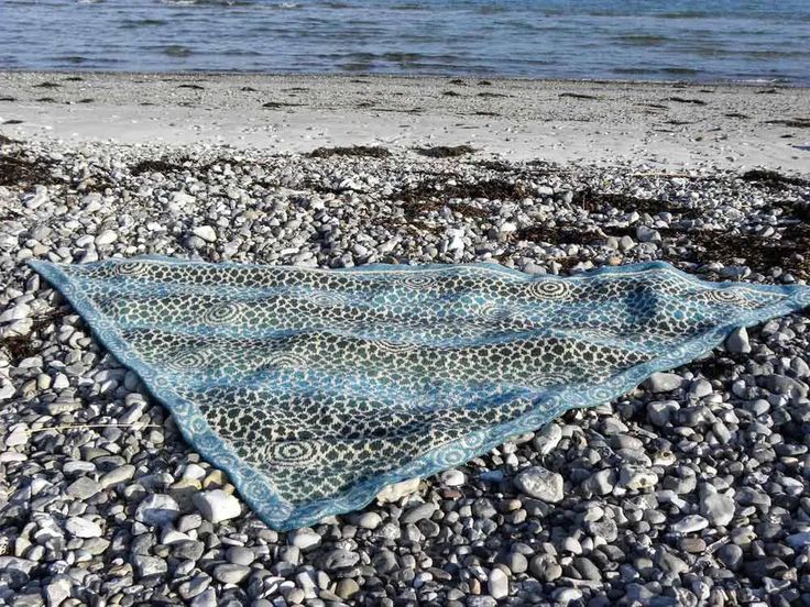 a blue blanket laying on top of a beach next to the ocean with rocks and pebbles