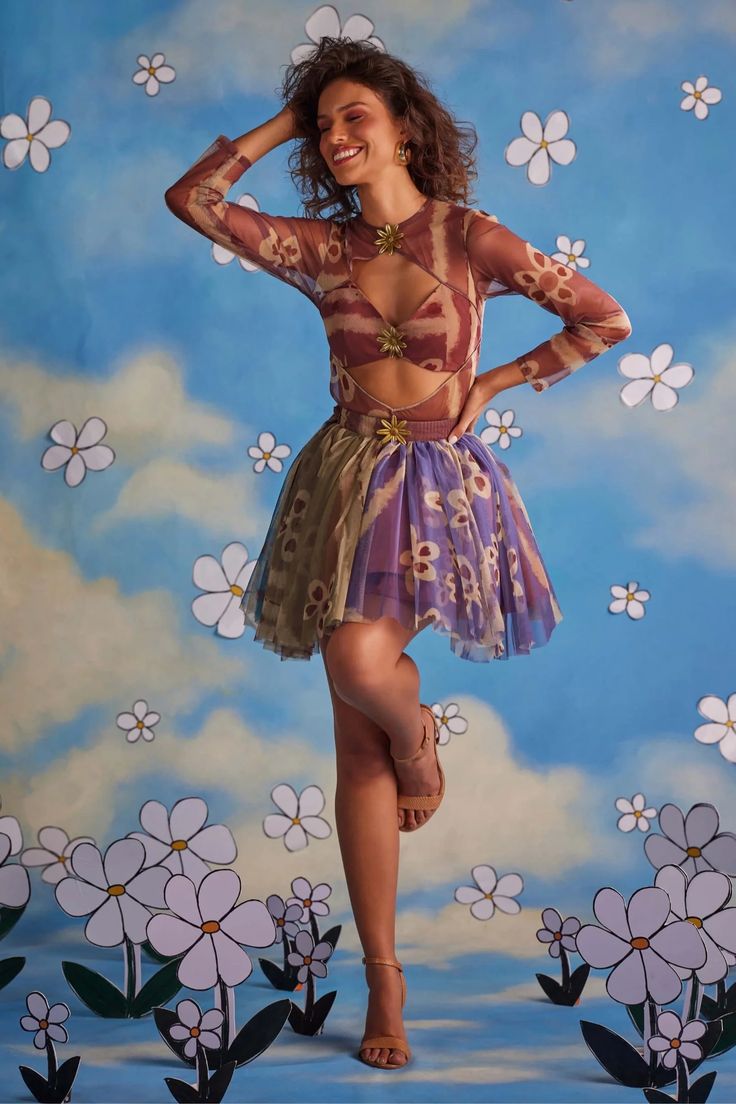 a woman posing in front of a painting with flowers on the wall and clouds behind her