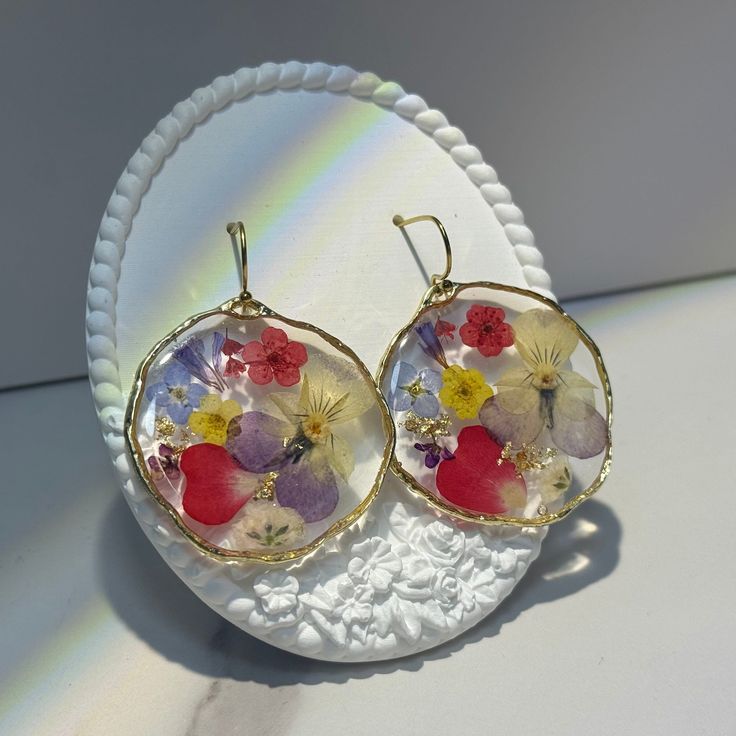 a pair of earrings with flowers on them sitting on a white doily plate in the sunlight