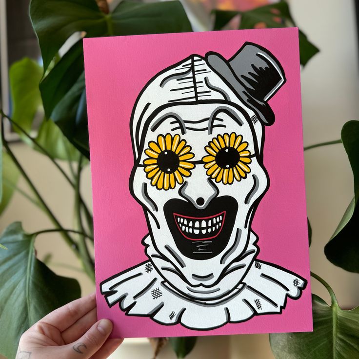 a hand holding up a pink card with a drawing of a skeleton wearing yellow flowers