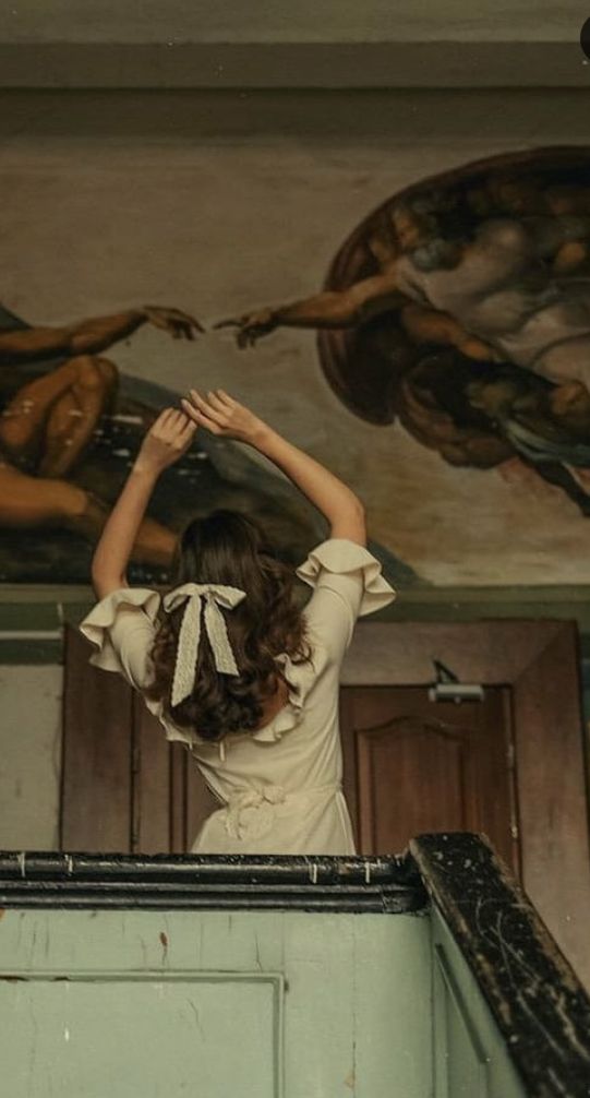 a woman standing on top of a balcony next to a painting above her head and hands in the air