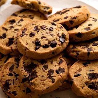 chocolate chip cookies piled on top of each other in a white plate with parchment paper